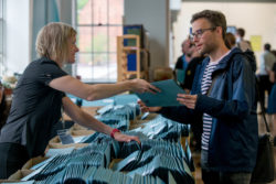 A female IMC staff member hands a registration pack to a male delegate.