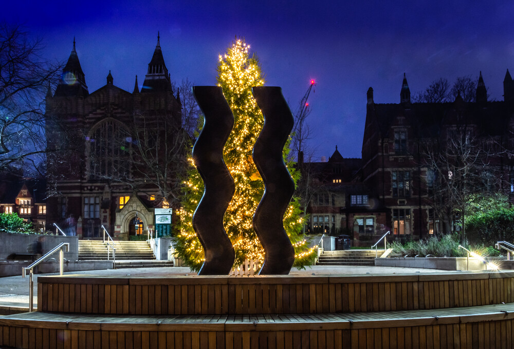 A picture of a brightly lit Christmas tree on campus with the towers of the Great Hall in silhouette behind