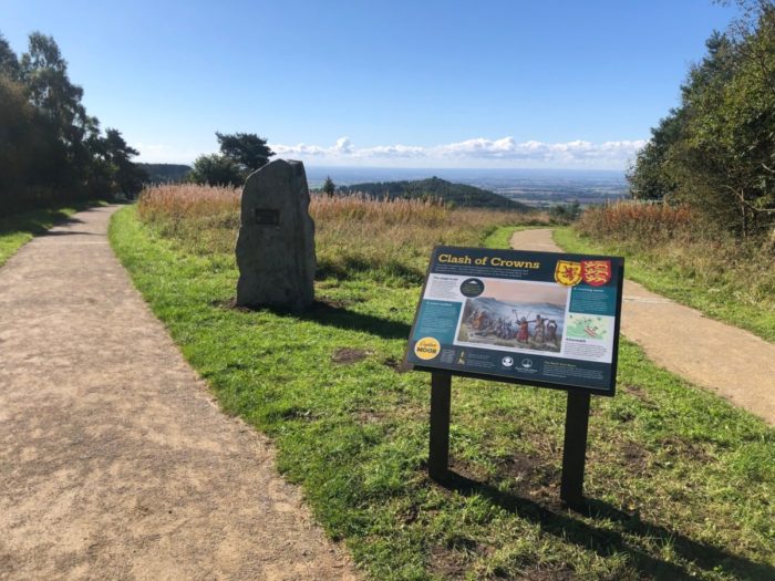 A view of Byland Battlefield in the Yorkshire Dales with rolling green country in the background and a commemorative plaque and information signage in the foreground on a bright sunny day.
