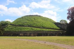 A photo of Tickhill castle mound, a low green earthwork against a blue sky.