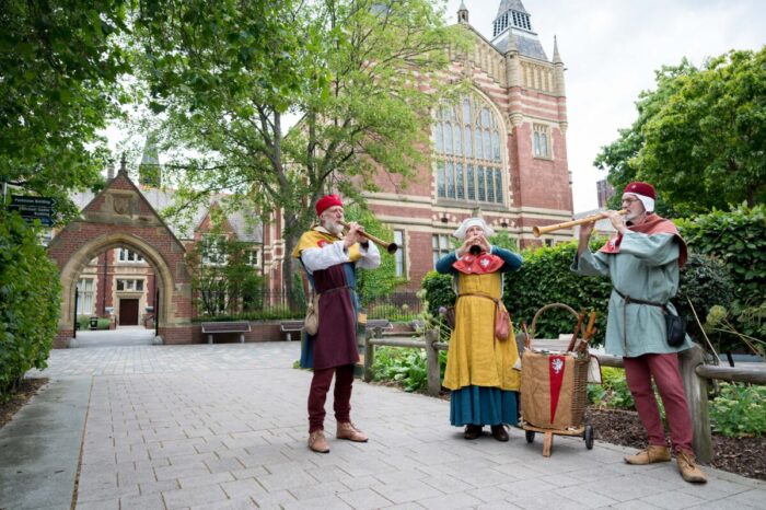 Three musicians stood playing their medieval instruments outside of the University of Leeds Great Hall. 