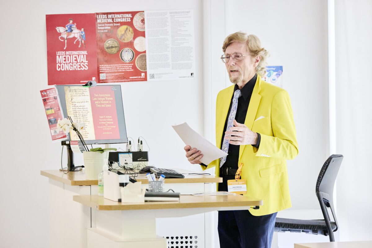 A speaker at IMC presenting a paper, dressed in a yellow jacket.